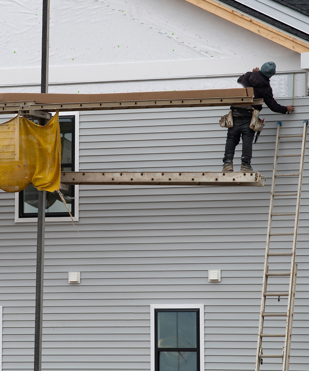 Construction worker installing insulated vinyl siding on a multi-story home, highlighting durability and professional craftsmanship.