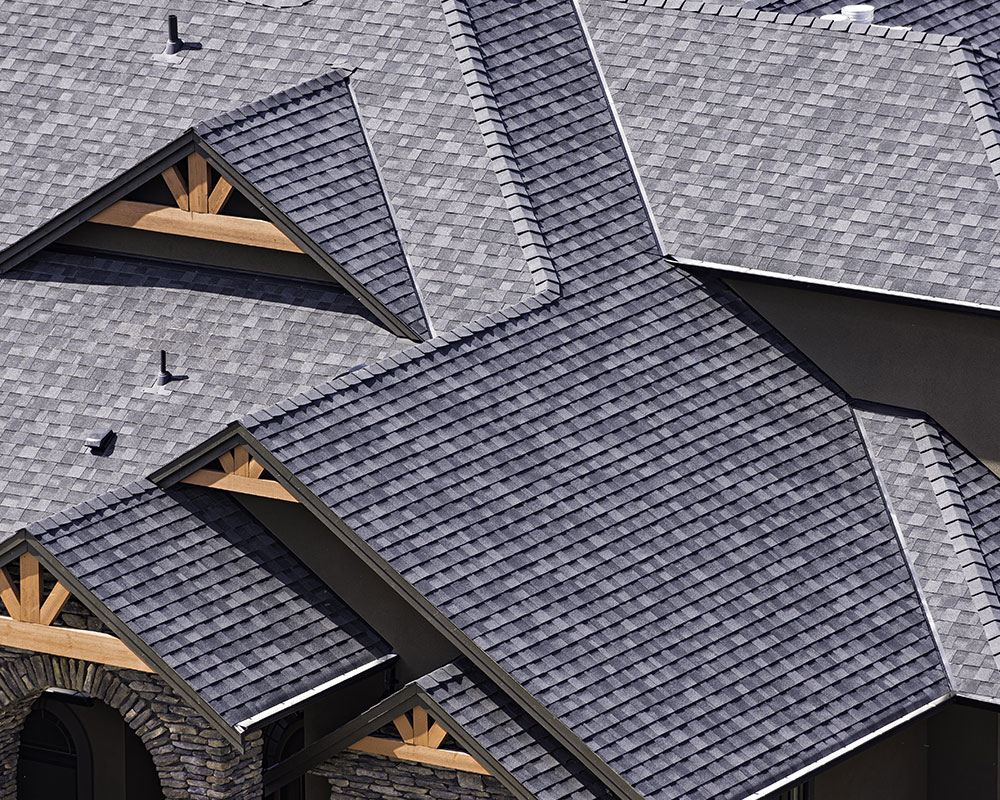 Close-up view of a modern, multi-pitched asphalt shingle roof on a luxury home with detailed gable accents.