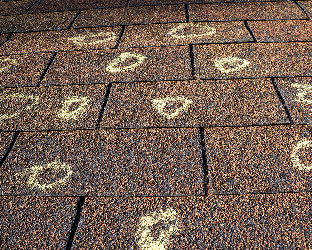 Close-up of storm-damaged shingles that need to be repaired in Springfield, MO, showcasing Roof For Less's prompt and reliable storm damage repair services.